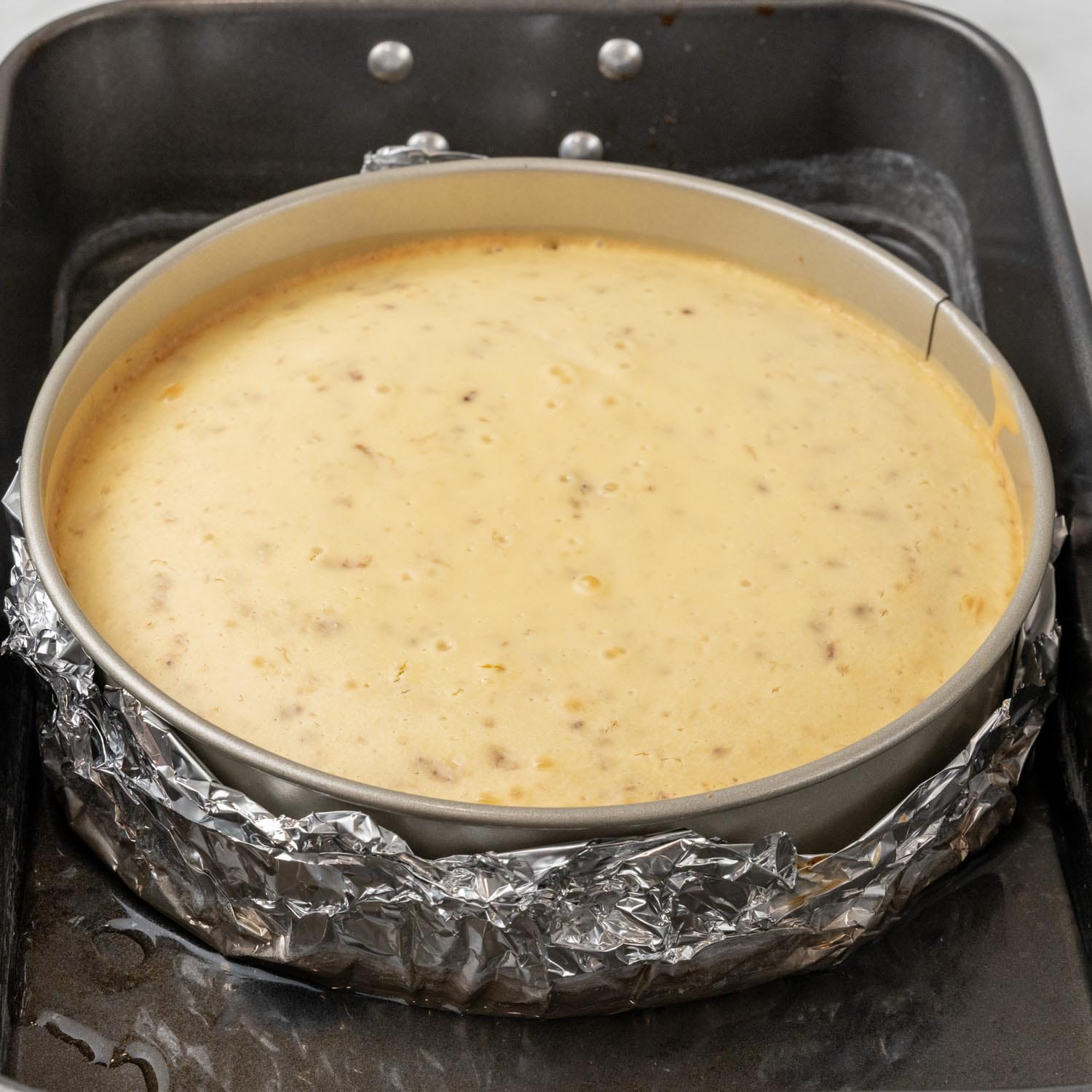 banana cheesecake in a pan, wrapped in foil and placed in a water bath for baking.