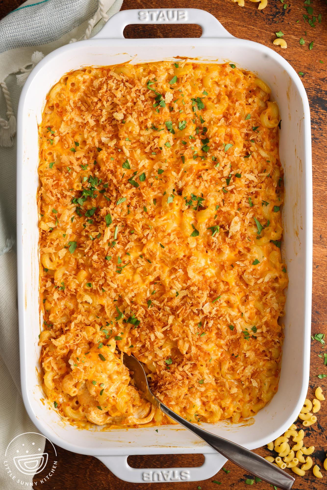 a 9x13 pan of buffalo chicken mac and cheese on a wooden surface. a metal spoon is about to serve it.