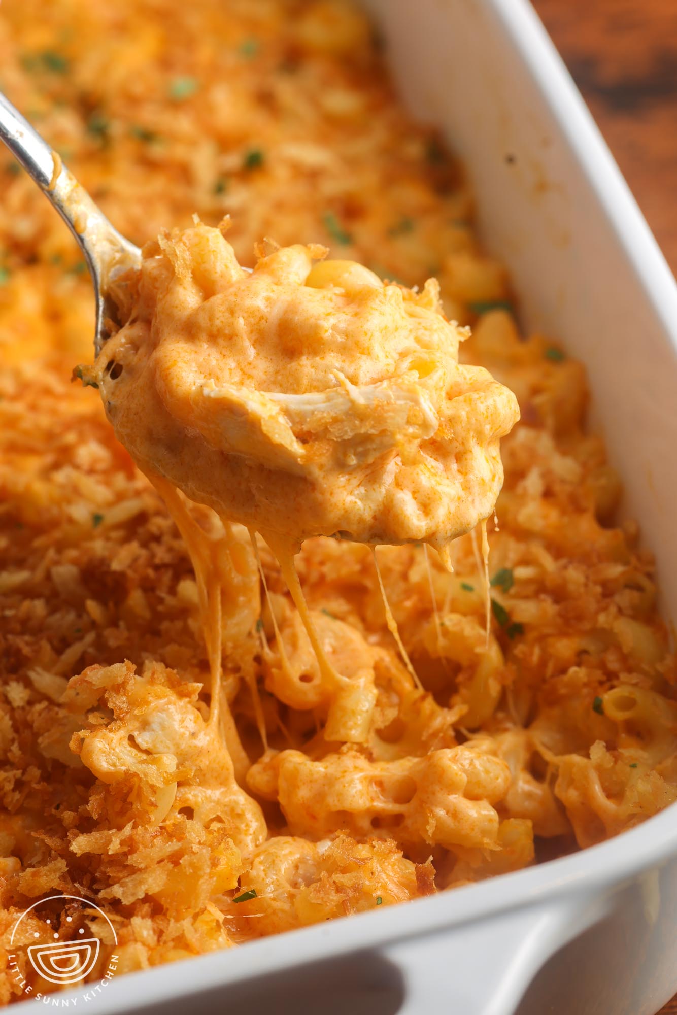 closeup of buffalo chicken mac and cheese. A spoon is lifting a bite from the pan, showing the thick and melty cheese sauce.