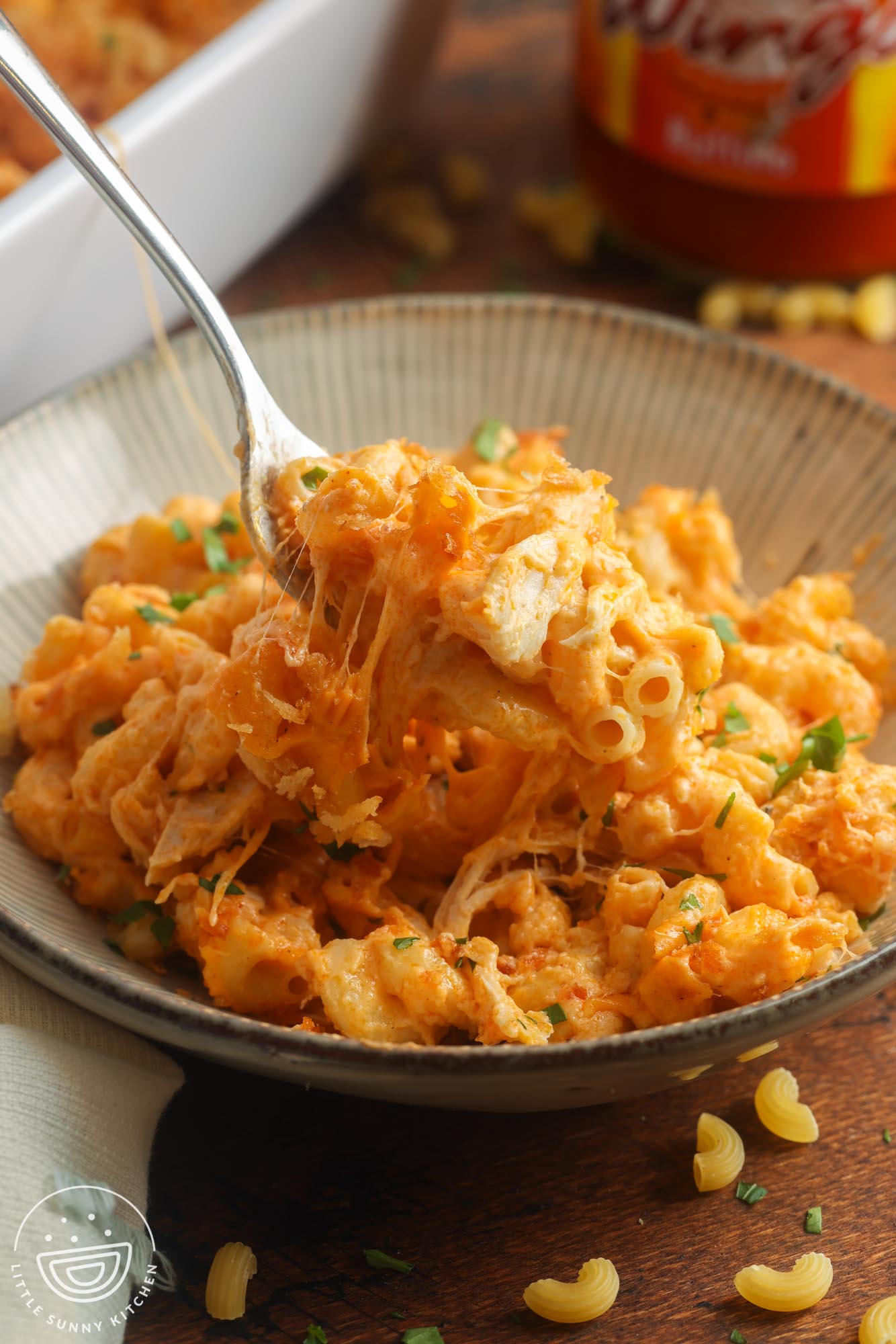 a serving of cheesy buffalo mac and cheese with chicken in a light green ceramic bowl with a fork.