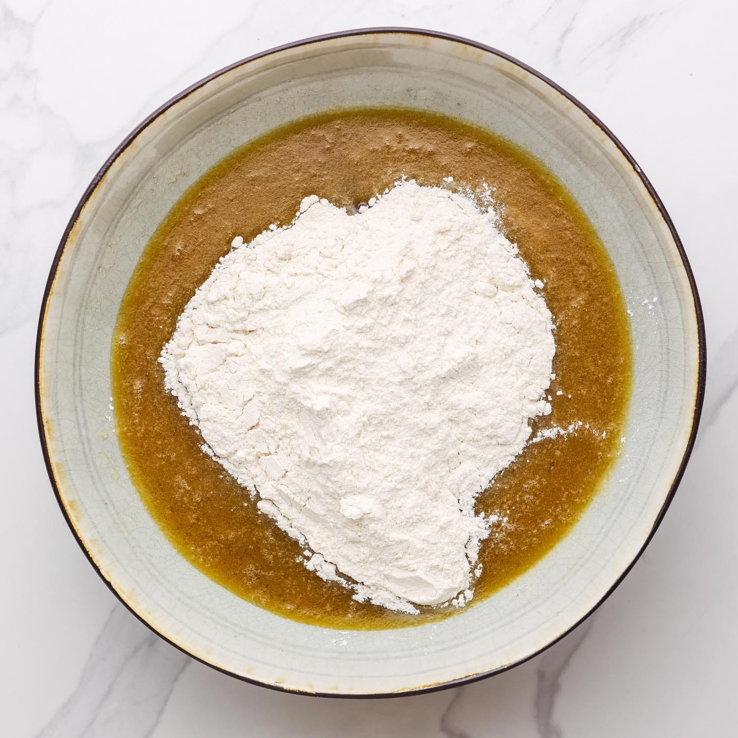 flour added to wet ingredients for date bread in a ceramic bowl.