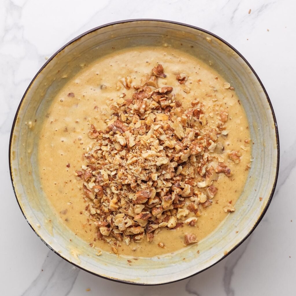 chopped toasted walnuts added to date bread batter in a ceramic bowl.