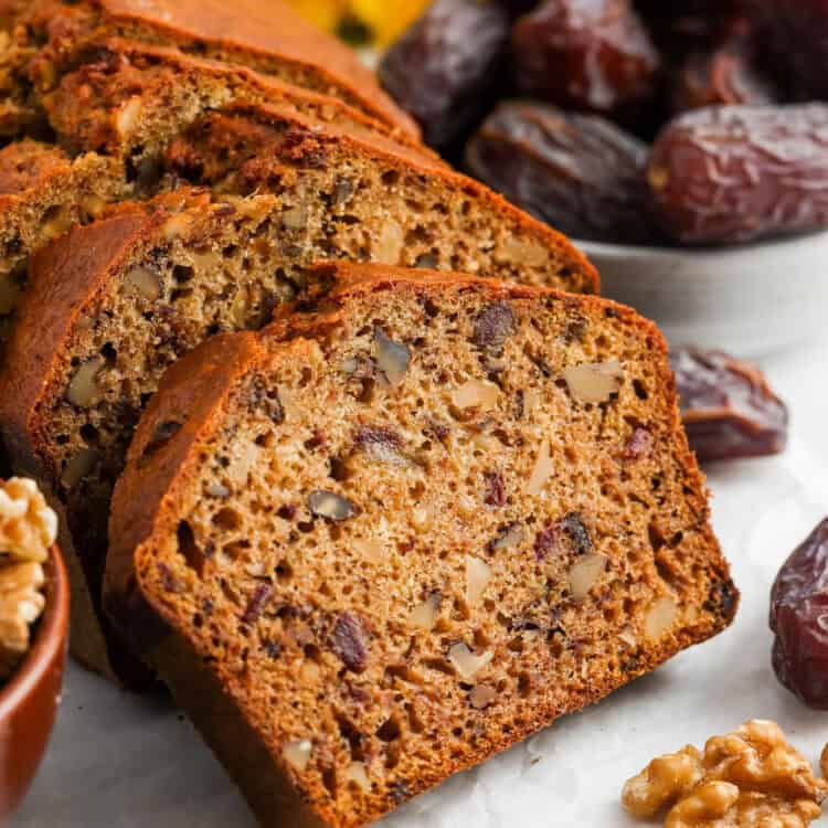 a loaf of date bread sliced to show the large pieces of walnuts and dried dates inside.