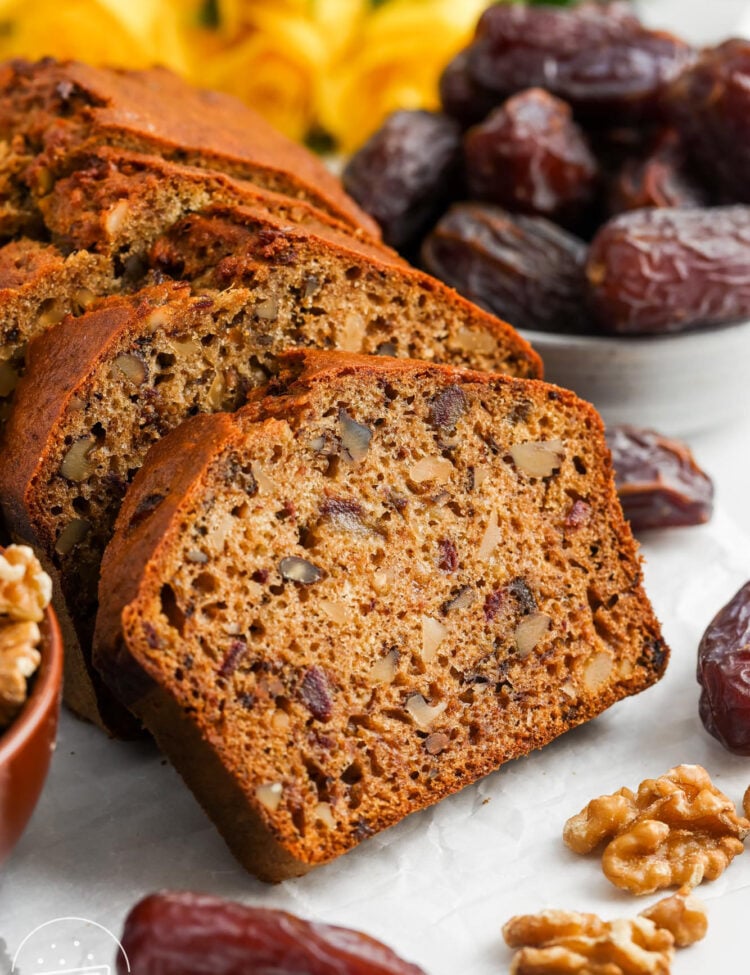 a loaf of date bread sliced to show the large pieces of walnuts and dried dates inside.