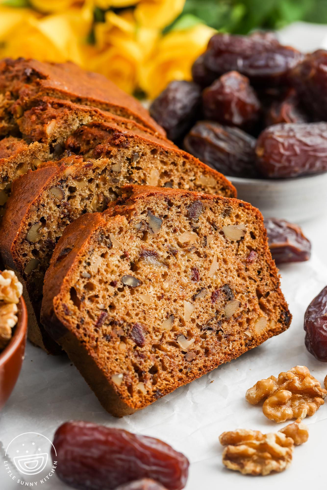 a loaf of date bread sliced to show the large pieces of walnuts and dried dates inside.