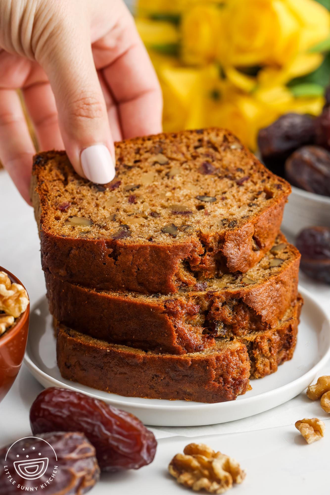 three slices of date walnut bread stacked on a plate. A hand is picking up the top slice.