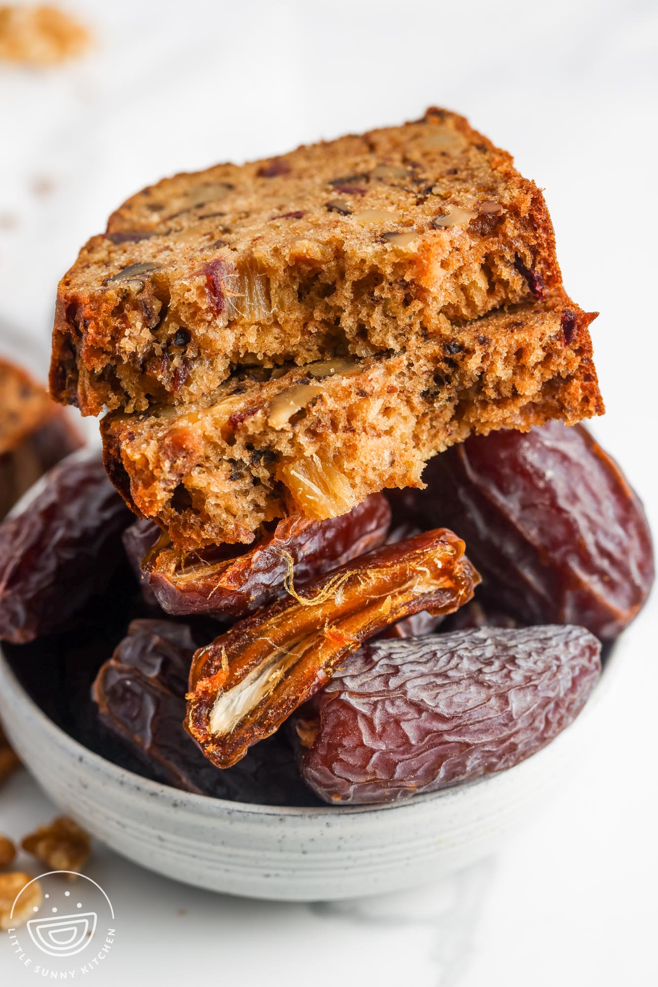 a slice of date nut bread torn in half, sitting on top of a bowl of dried dates.