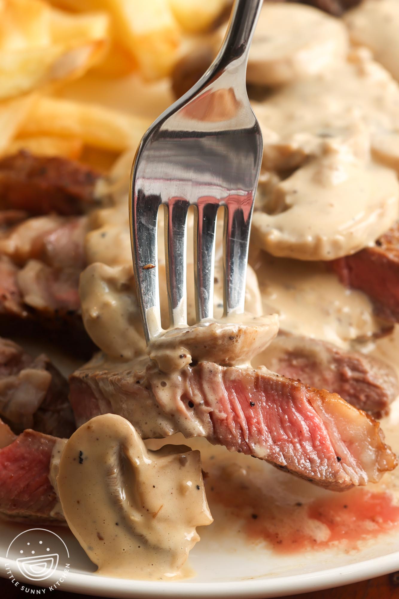 a fork holding a piece of steak with creamy mushroom sauce.