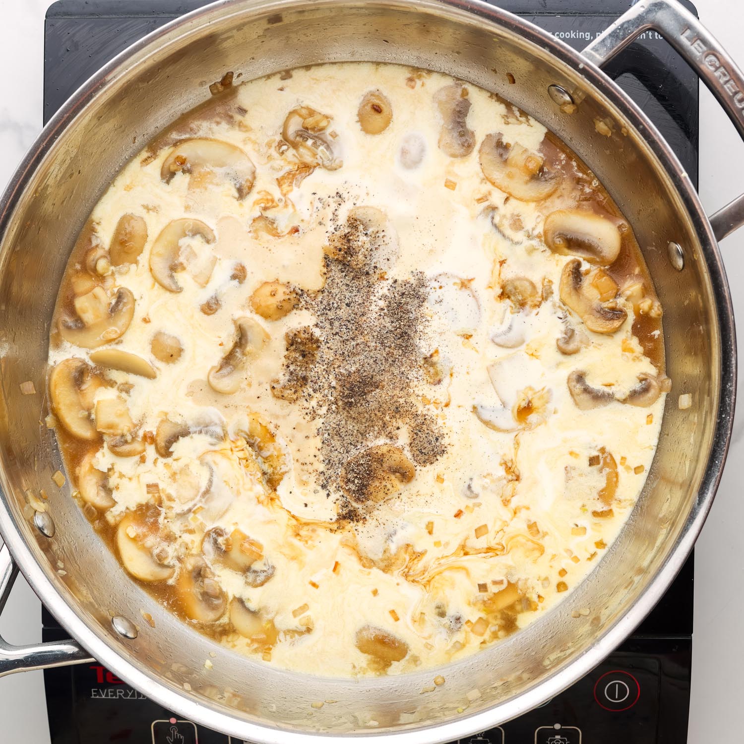 cream and seasonings added to mushroom sauce for steak in a metal skillet.