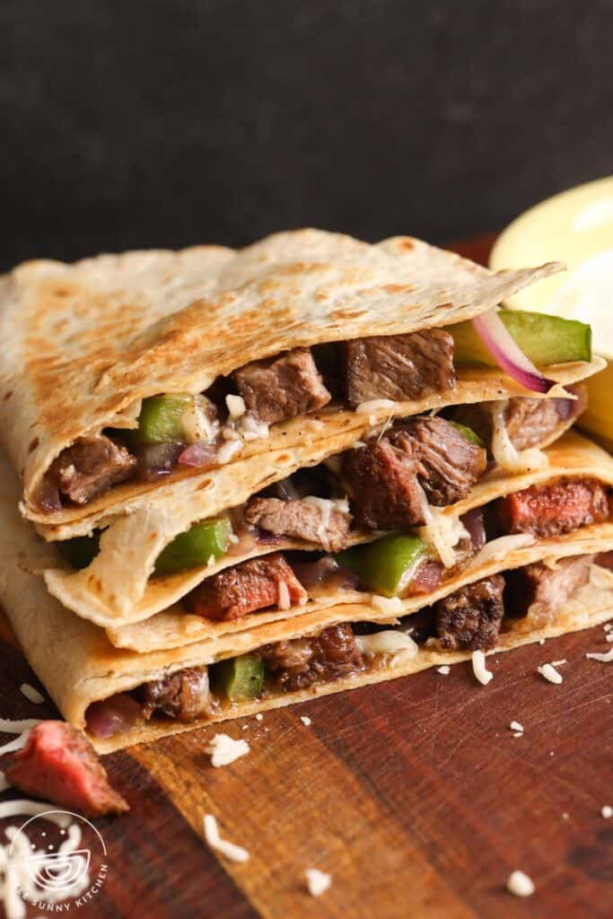 four wedges of steak quesadillas, stacked on a wooden cutting board.