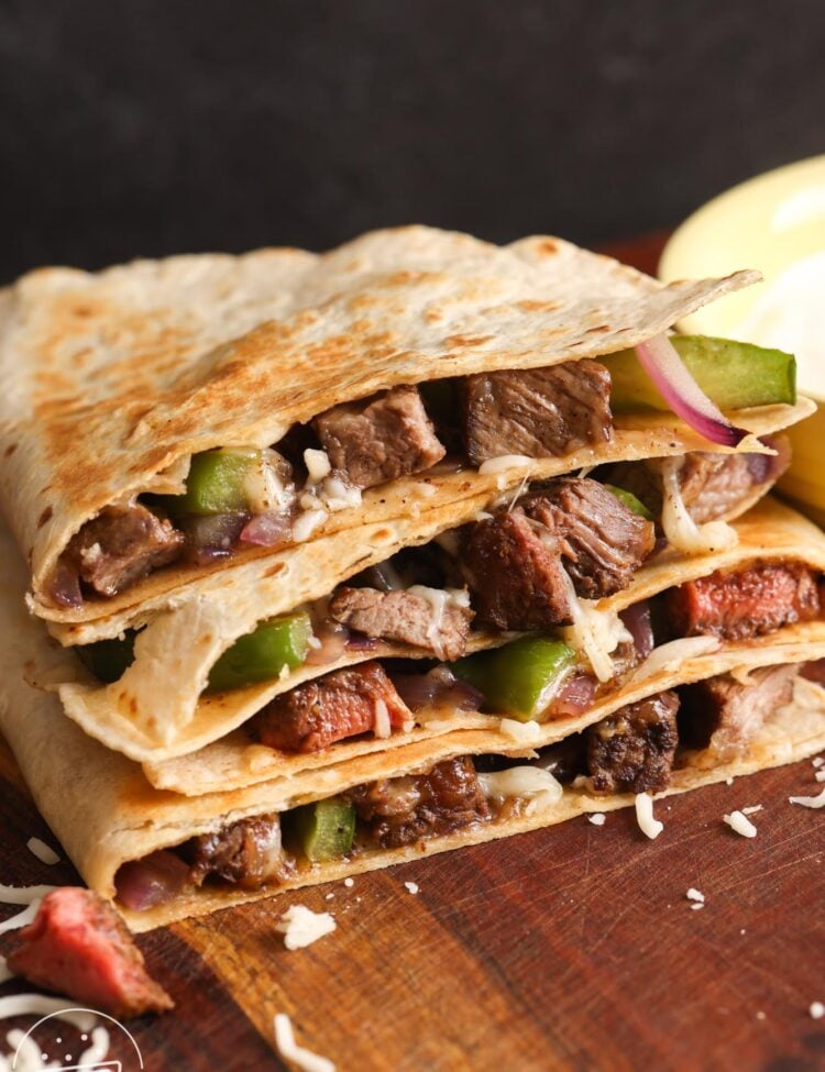 four wedges of steak quesadillas, stacked on a wooden cutting board.