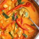 A stainless steel skillet of Thai red curry with chicken and red bell peppers, garnished with Thai basil leaves.
