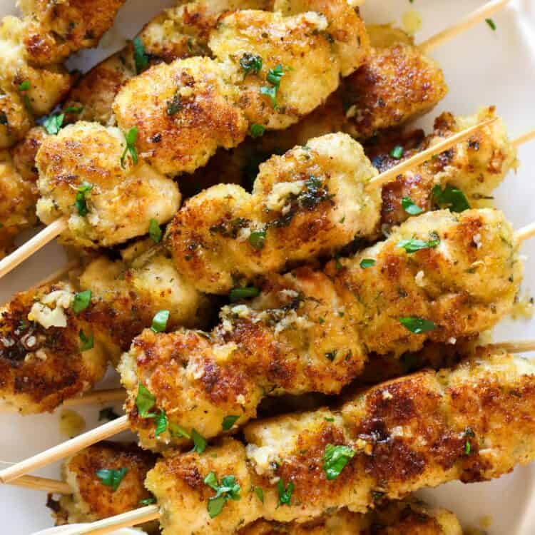 a platter of chicken spiedini skewrs with a side of sauce.