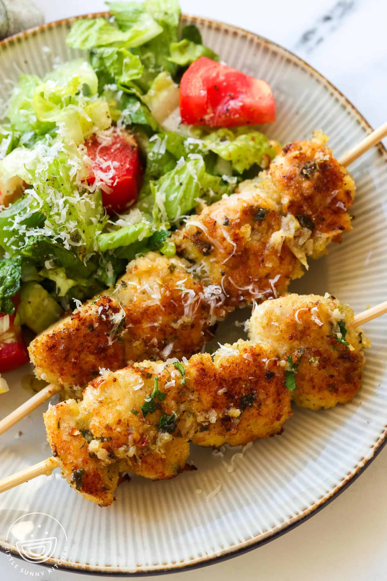 a dinner plate with a fresh lettuce and tomato salad and two spiedini chicken skewers.