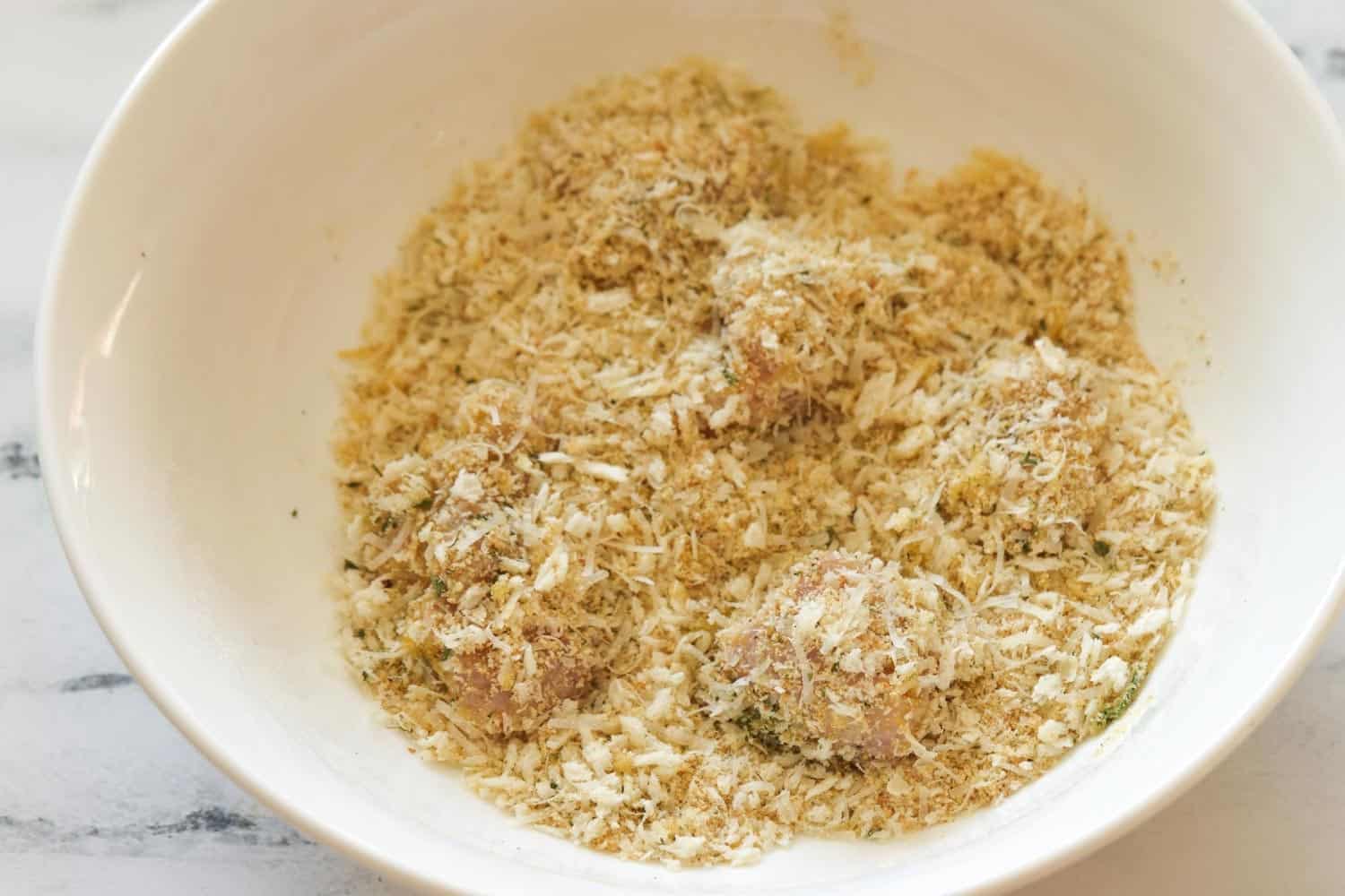 marinated chicken pieces in a bowl with breadcrumbs.