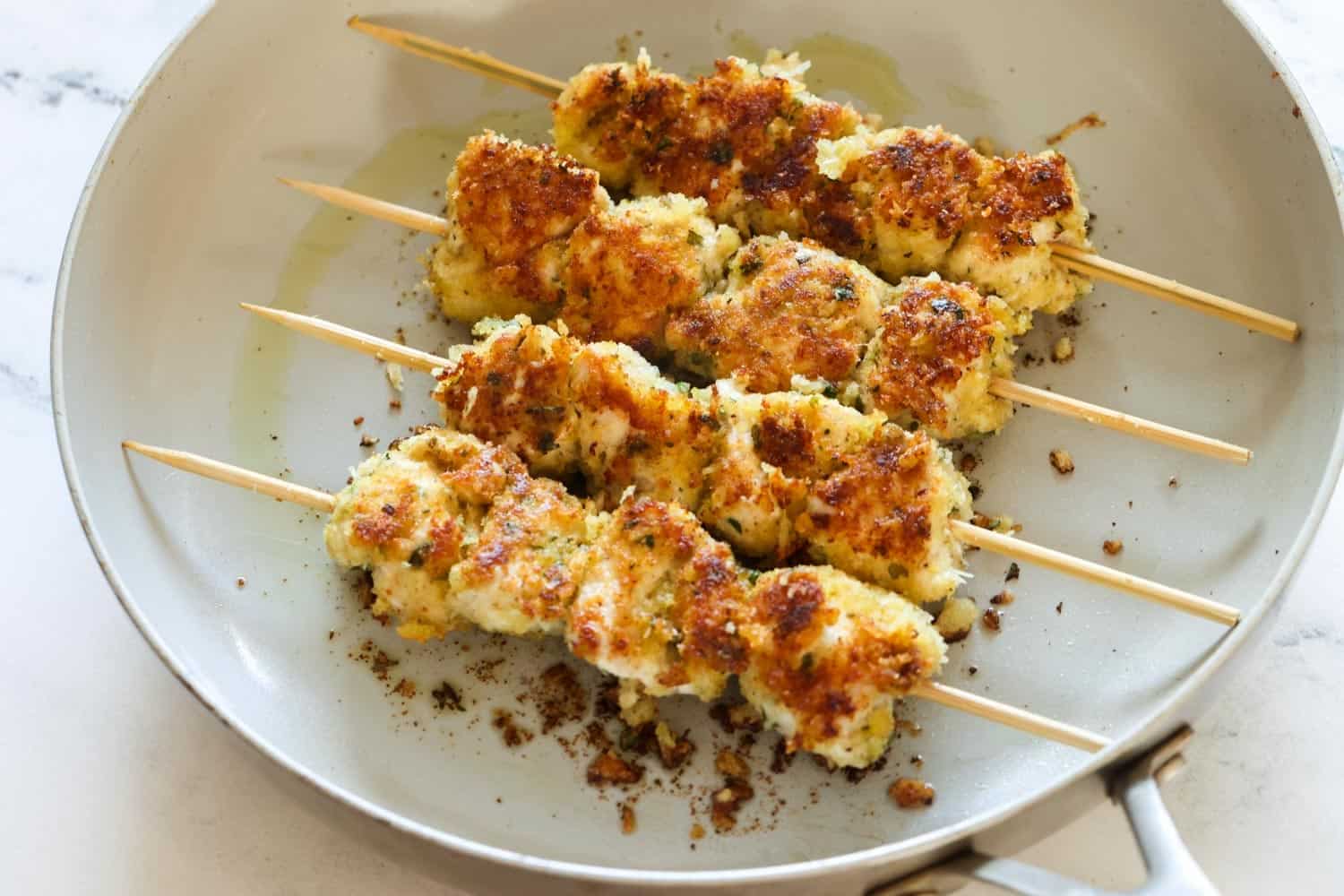 pan seared chicken spiedini skewers with crispy breadcrumb coating in a ceramic frying pan.