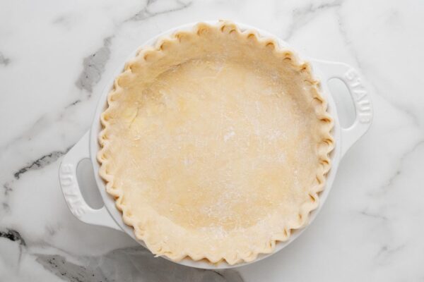 pie crust dough pressed into a white pie pan, edges are fluted.