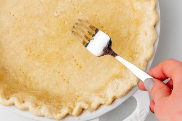 a fork poking holes into a partially baked pie crust.