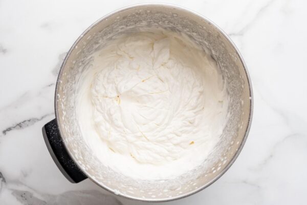whipped cream topping in the bowl of a stand mixer, set on a marble counter.