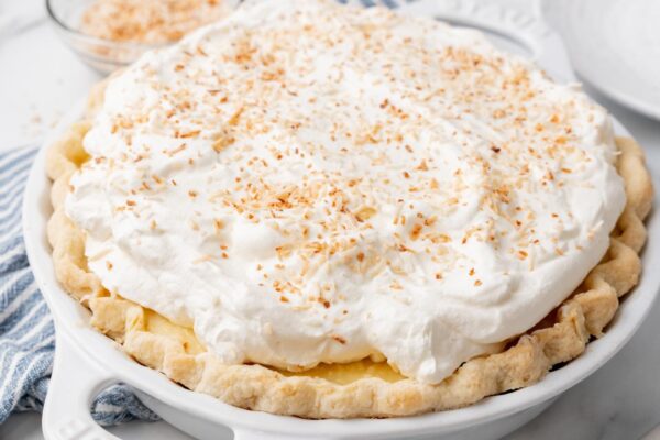 a whole coconut cream pie topped with homemade whipped cream and toasted coconut shreds.