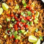 overhead view of Mexican rice with beef, beans, and corn in a skillet. The dish is topped with fresh salsa made with avocado, onion, and tomatoes.