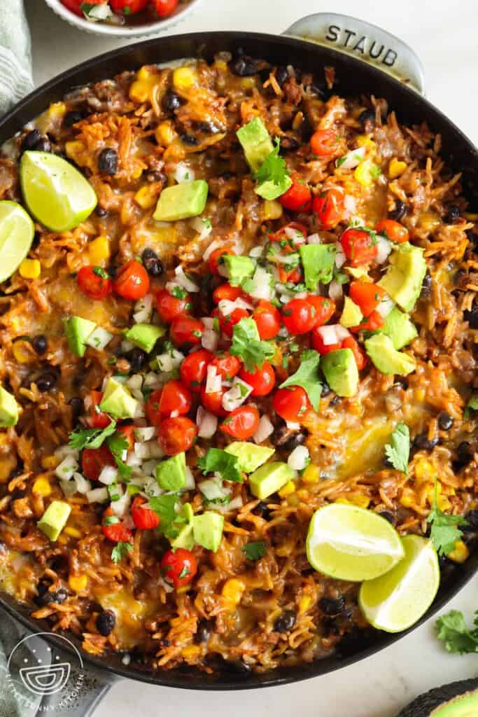overhead view of Mexican rice with beef, beans, and corn in a skillet. The dish is topped with fresh salsa made with avocado, onion, and tomatoes.