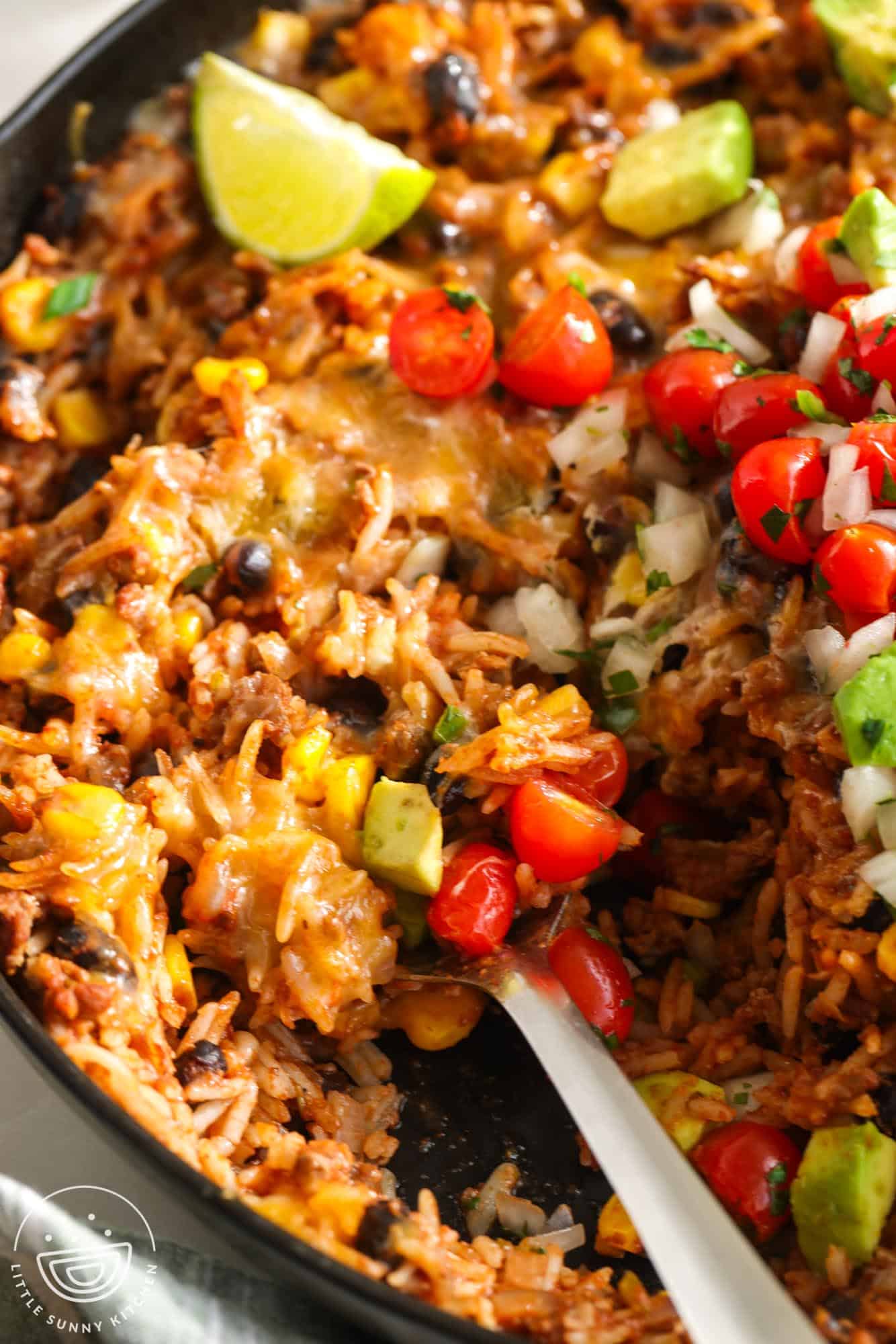 A skillet meal of mexican rice with beef and beans, topped with fresh tomatoes, avocado, and lime.