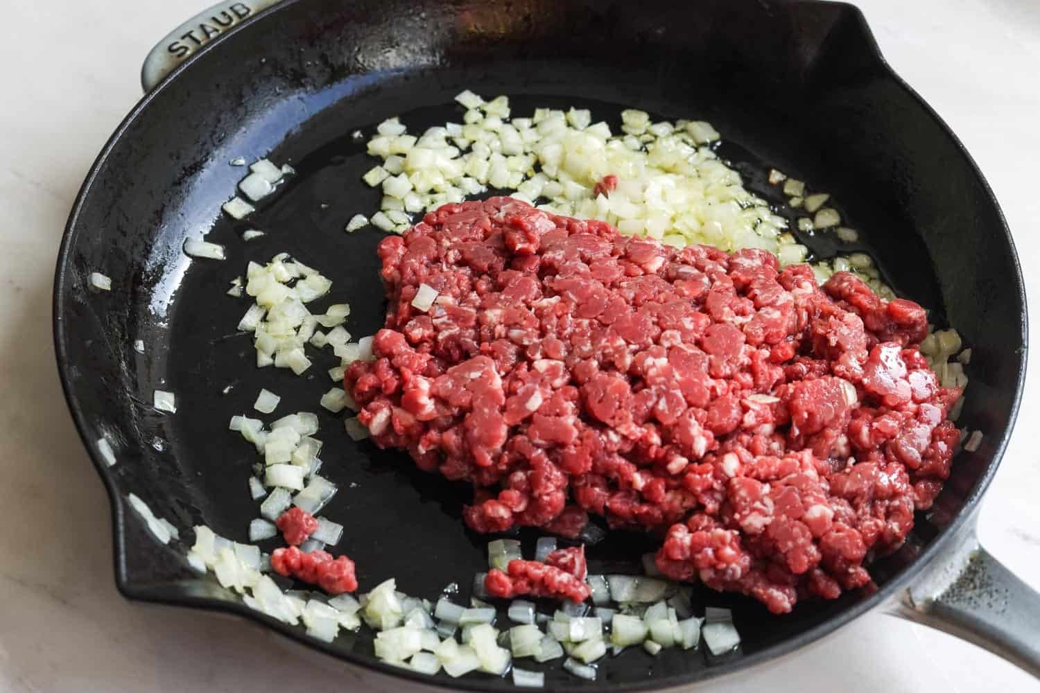 Diced onions and fresh ground beef cooking in a cast iron skillet.