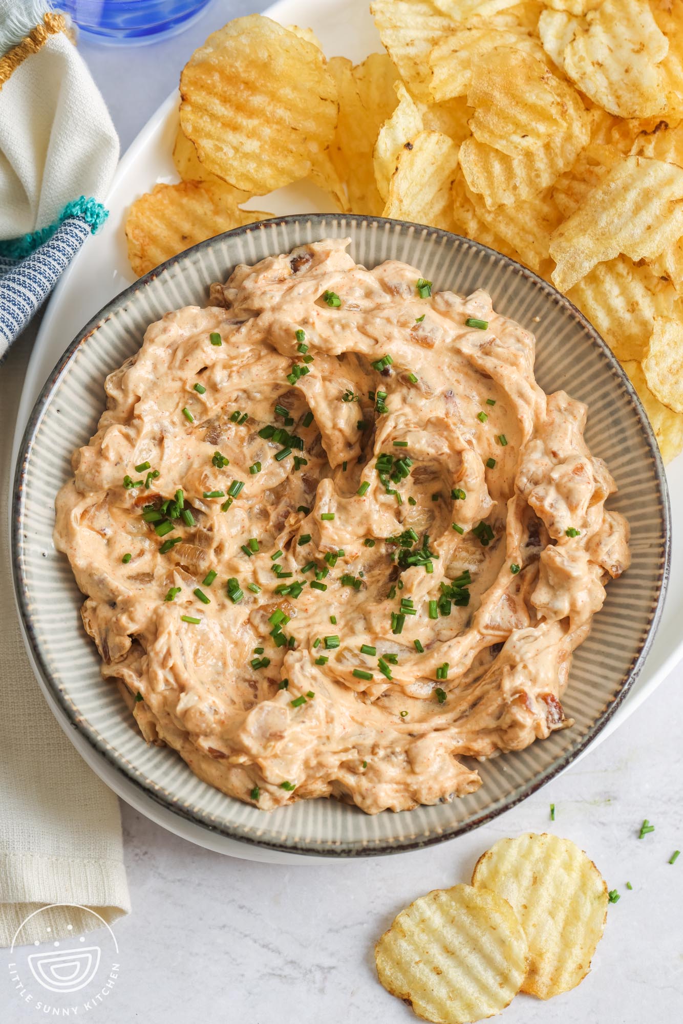 a platter of potato chips with a large bowl of homemade caramelized onion dip on the left side.