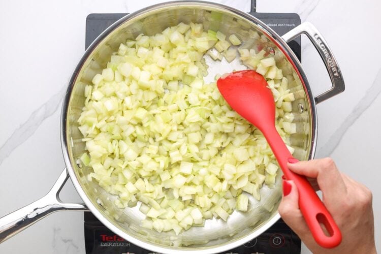diced onions cooking in a skillet, stirred with a red spatula.