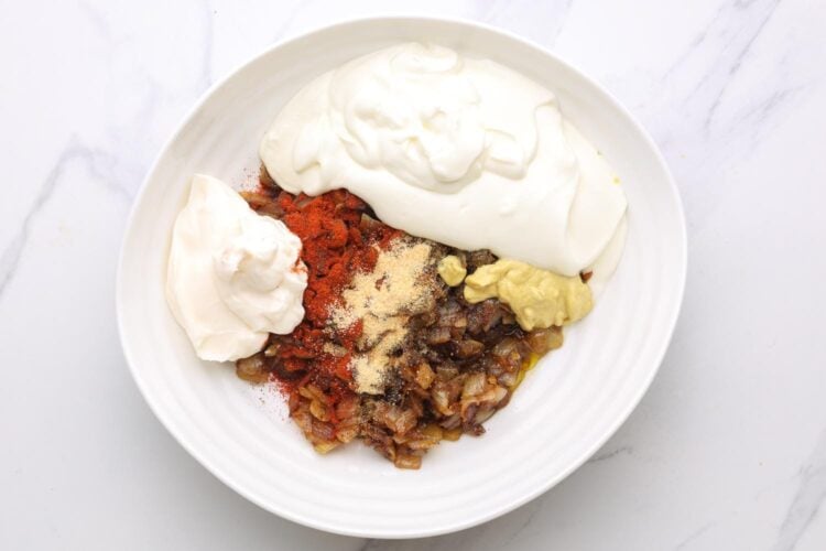 sour cream, mayo, and seasonings added to a bowl of caramelized onions to make a dip.