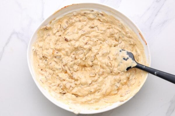 caramelized onion dip in a white mixing bowl, stirred with a black spatula.