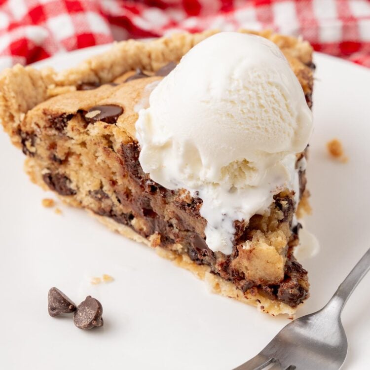 a warm slice of chocolate chip cookie pie topped with a scoop of vanilla ice cream. A fork is on the plate in front of the slice.
