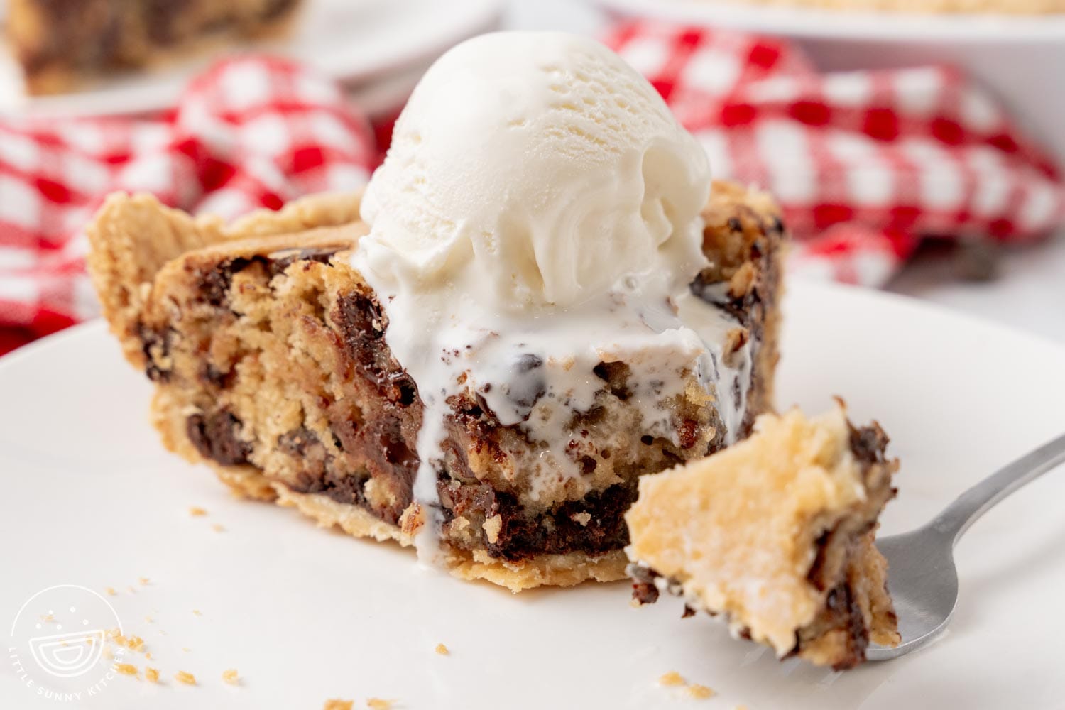 closeup of a slice of chocolate chip cookie pie, topped with melty vanilla ice cream.