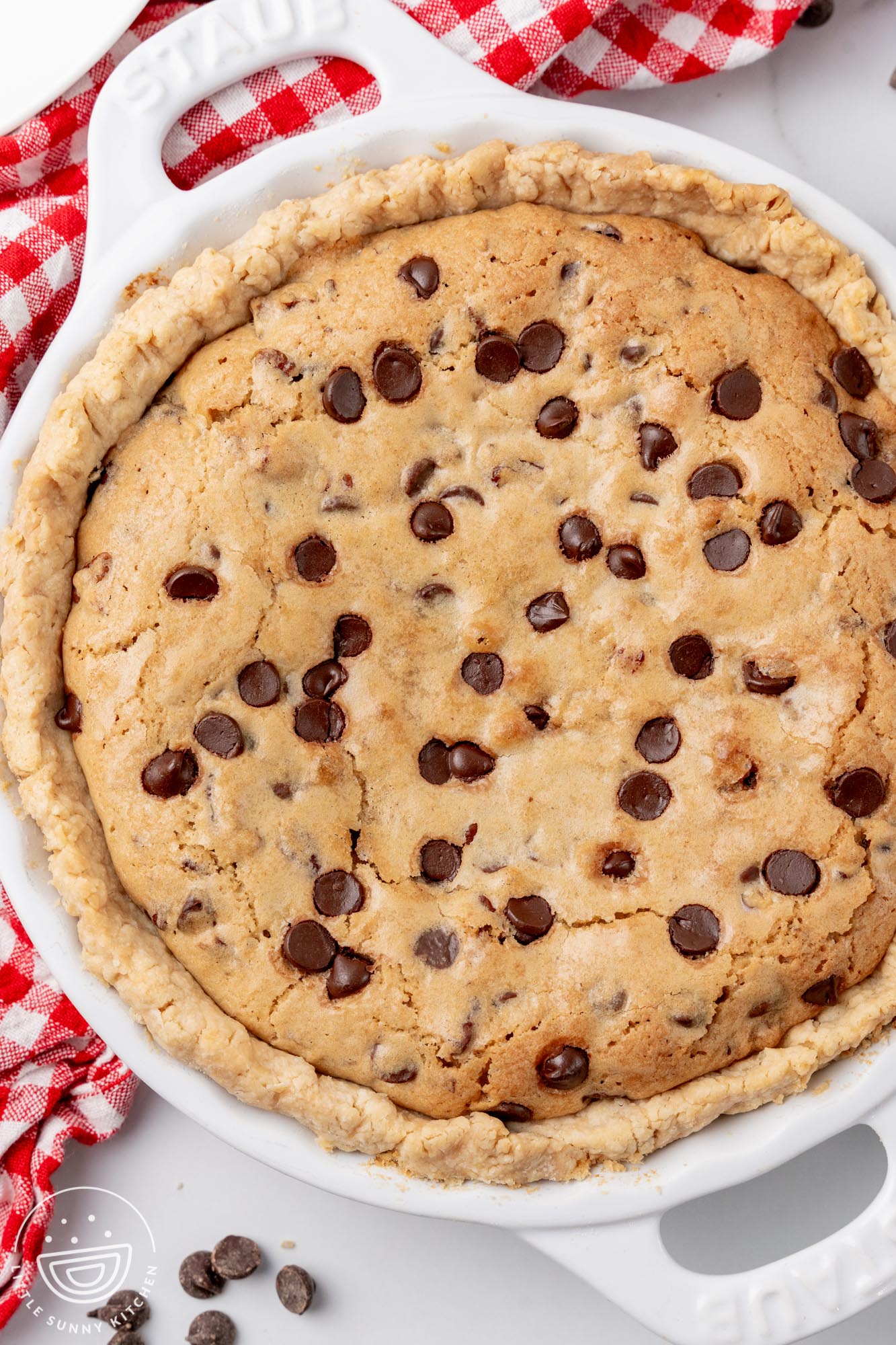 Baked cookie pie with homemade crust in a white pie pan. Under the pie is a red and white checkered napkin.
