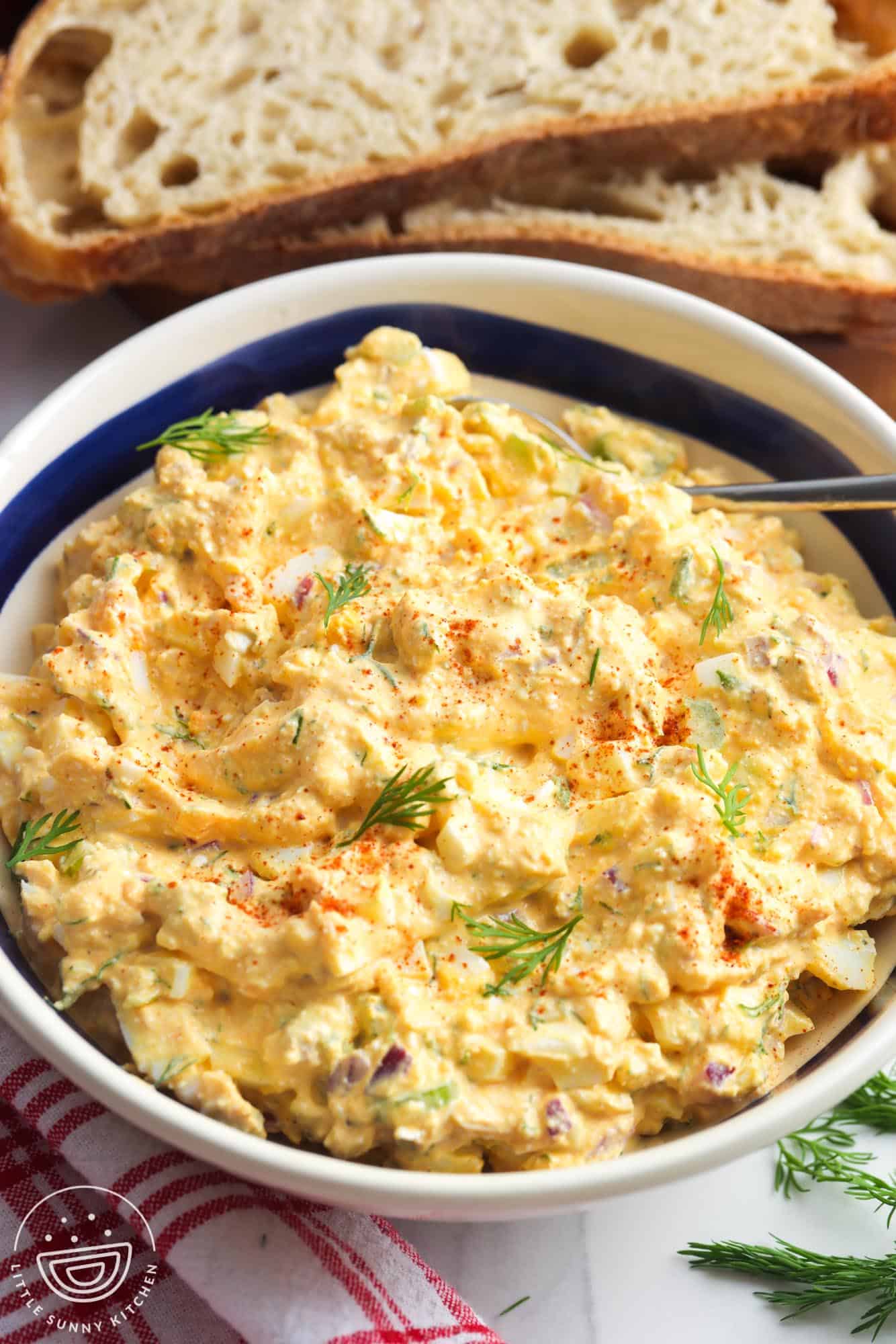 a large bowl of cottage cheese egg salad garnished with dill and paprika, in front of slices of bread.