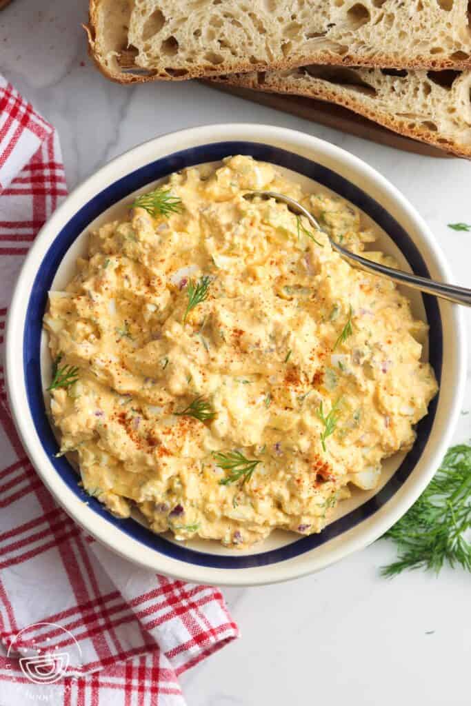 overhead view of a large bowl of egg salad with cottage cheese and dill next to slices of fresh bread.