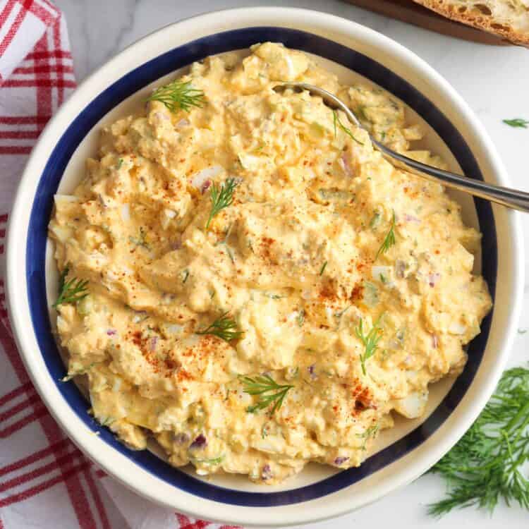 overhead view of a large bowl of egg salad with cottage cheese and dill next to slices of fresh bread.