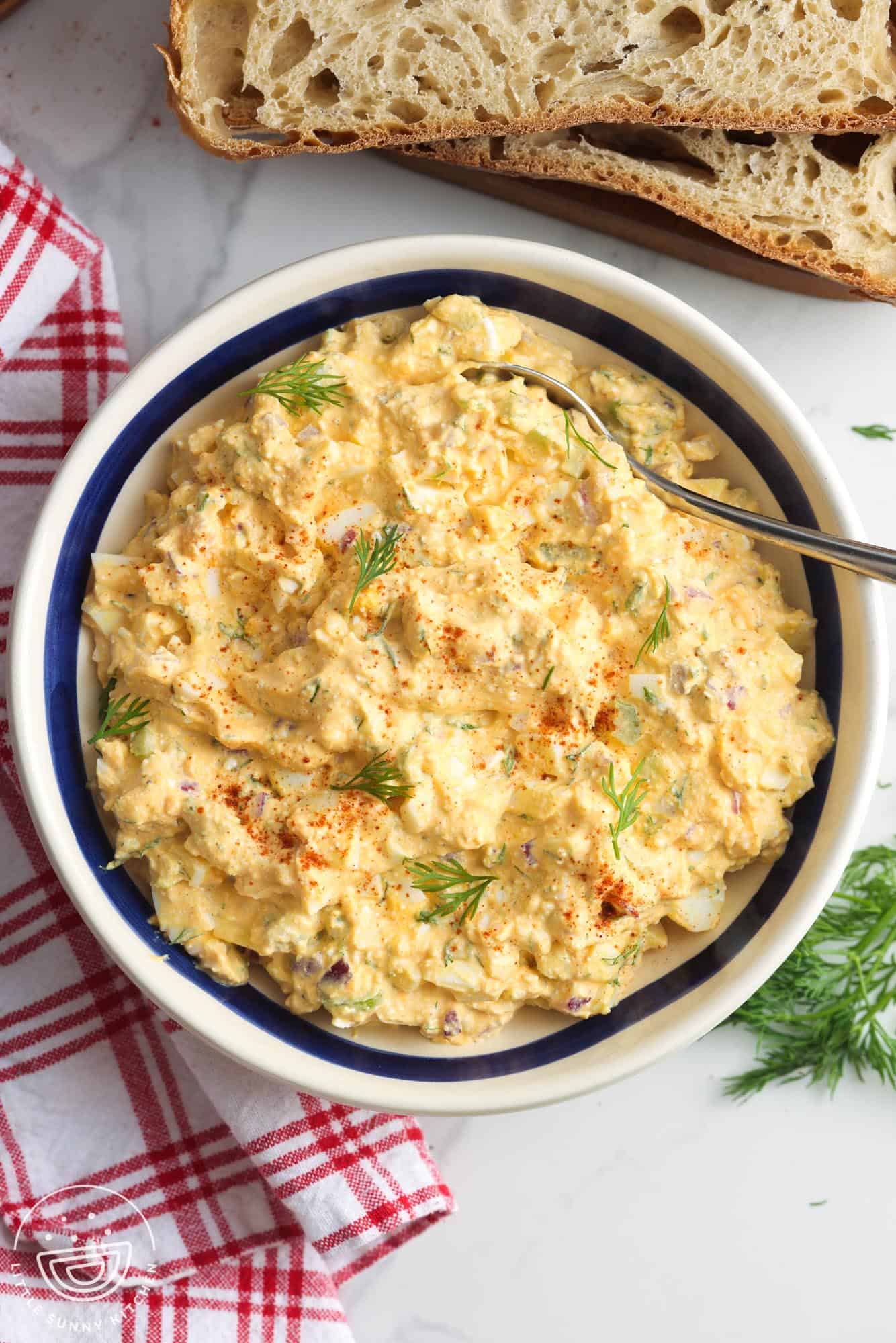 overhead view of a large bowl of egg salad with cottage cheese and dill next to slices of fresh bread.