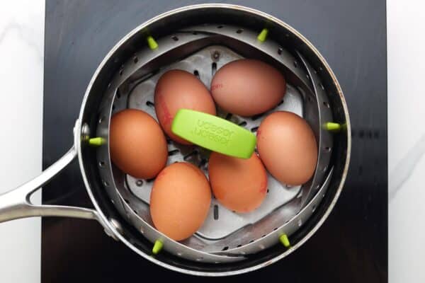 six brown eggs steaming in a saucepan.