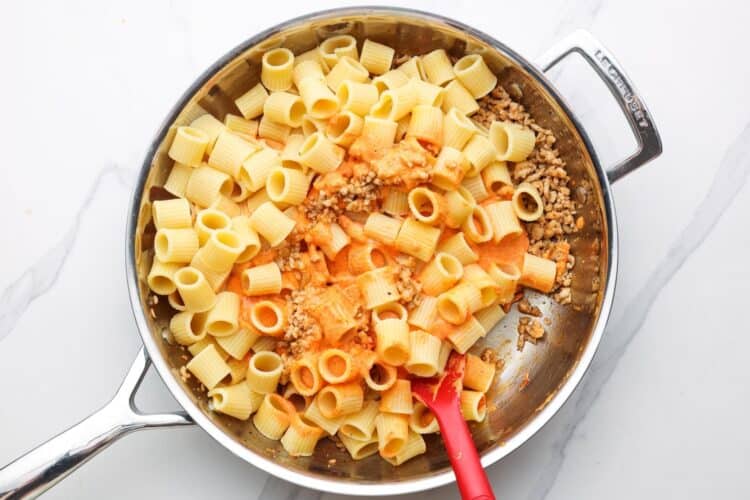 pasta and cottage cheese sauce added to ground chicken in a stainless steel skillet.