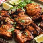a large green platter of grilled chili lime chicken thighs garnished with lime wedges and fresh cilantro.