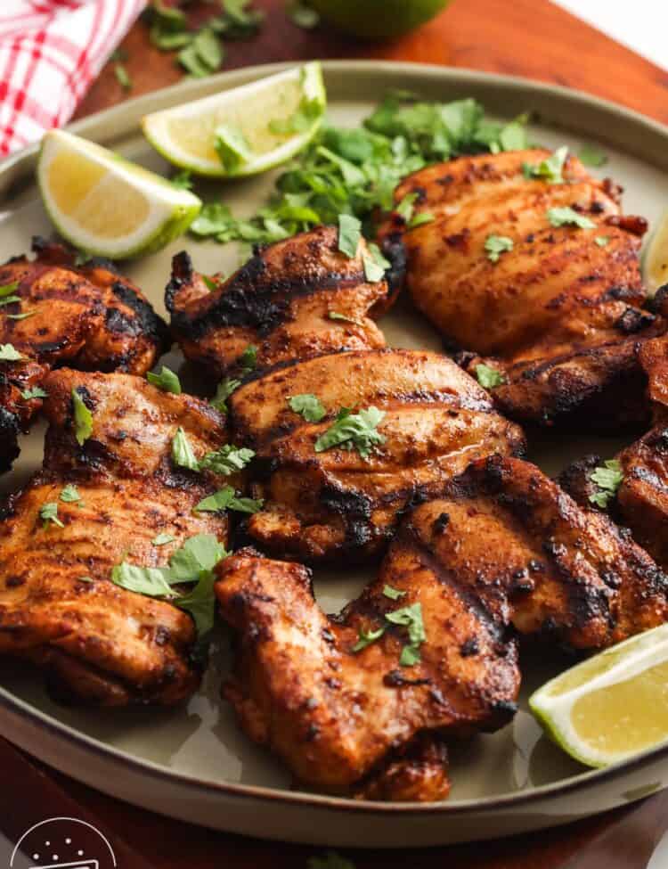 a large green platter of grilled chili lime chicken thighs garnished with lime wedges and fresh cilantro.