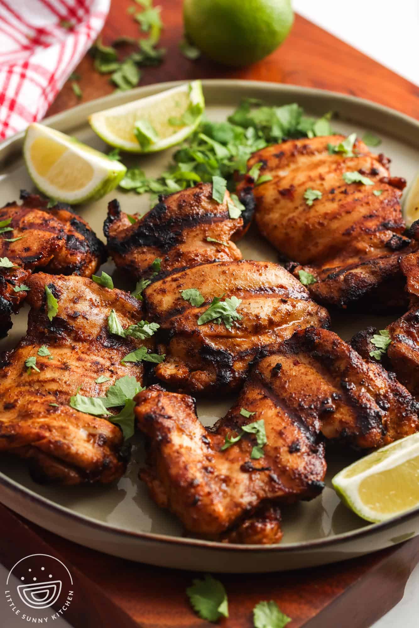 a large green platter of grilled chili lime chicken thighs garnished with lime wedges and fresh cilantro.