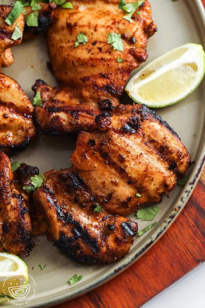 closeup of grilled chili lime chicken on a light green platter with lime wedges on the side.