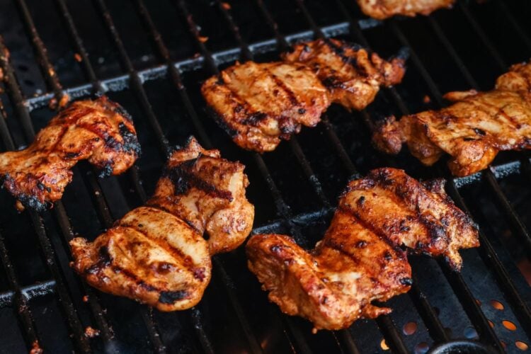 boneless, skinless, marinated chicken thighs cooking on a gas grill.