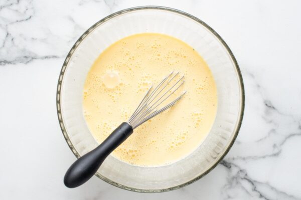 Egg and cream mixture for quiche, whisked together in a glass bowl.