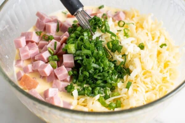 white cheddar cheese, diced ham, and green onion stirred into quiche mixture, closeup view.