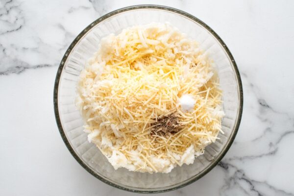 thawed frozen hash browns, parmesan cheese, seasonings, and butter in a glass bowl.