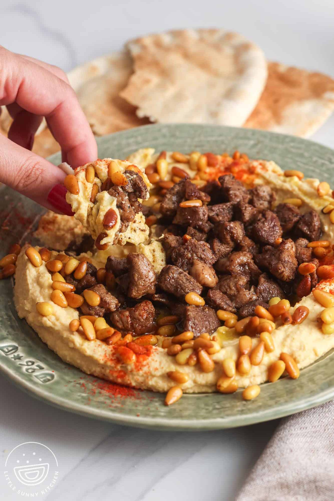 Dipping a piece of pita bread in hummus with meat and pine nuts